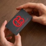 A hand holding a black business card with a red logo.